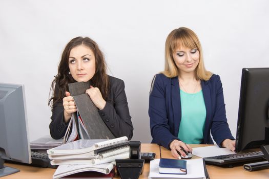 Two young beautiful girls colleagues sitting at the same desk in the office