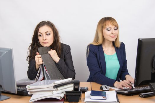 Two young beautiful girls colleagues sitting at the same desk in the office