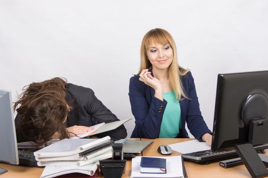 Two young beautiful girls colleagues sitting at the same desk in the office