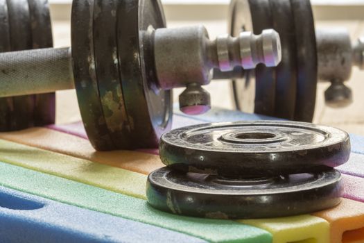 Sports dumbbells and black pancakes on striped rug