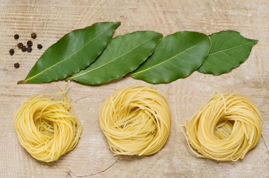 No cooked pasta, Bay leaf and black pepper, old wooden background