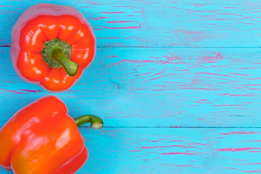 Pair of large orange color bell peppers on one side of blue wooden table background with copy space