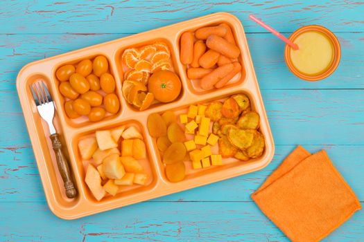 Top down first person perspective view of rectangular serving tray filled with various vegetables and fruit next to fork, cup and napkin over blue wooden table