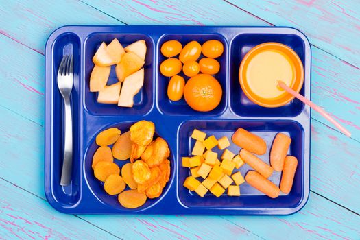 Assorted fresh and dried fruit cut into small pieces and juice in orange colors on blue plastic tray with stainless steel fork over wooden blue table