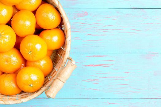 Top down first person perspective view of straw basket filled with clementine oranges over painted blue wooden table and copy space