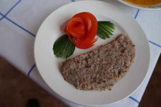 Buckwheat porridge with vegetables, red tomatoes and green cucumbers on a white plate