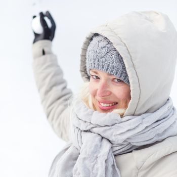 Cute casual young woman throwing snowball in winter time.