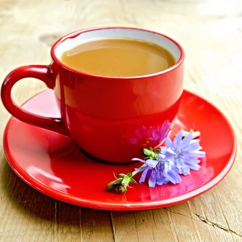 Chicory drink in a red cup with flower on a wooden boards background