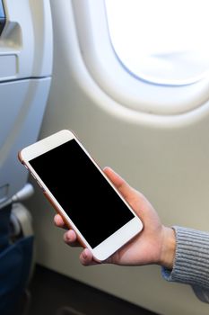 Woman holding digital mobile phone at airplane