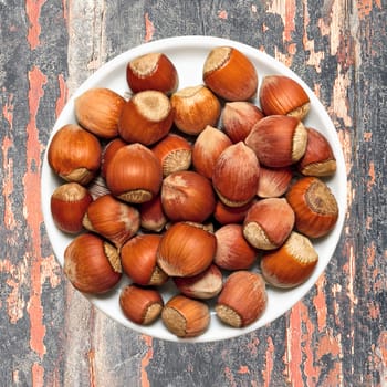 Hazelnuts in a white plate on old wooden background. With layers of paint.
