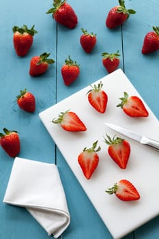 Wild strawberries placed on blue wooden background and illuminated with natural light