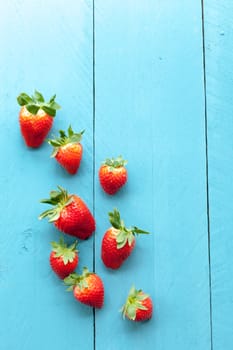 Wild strawberries placed on blue wooden background and illuminated with natural light