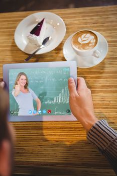 Smiling teacher gesturing thumbs up in front of blackboard against man holding tablet computer at table in cafe