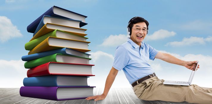 Portrait of cheerful man using laptop while listening music against stack of books against sky