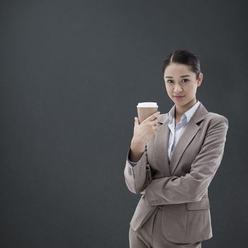 Portrait of a businesswoman holding a takeaway tea against grey background