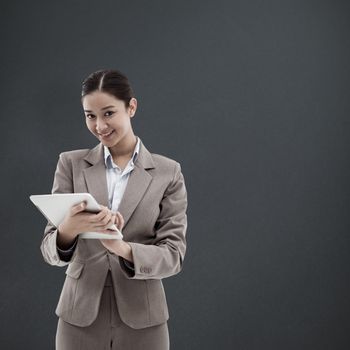 Portrait of a smiling businesswoman using a tablet computer against grey background