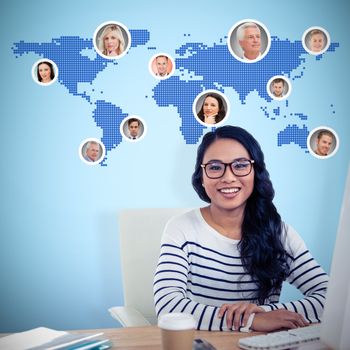 Smiling Asian woman sitting at desk posing for camera against blue background