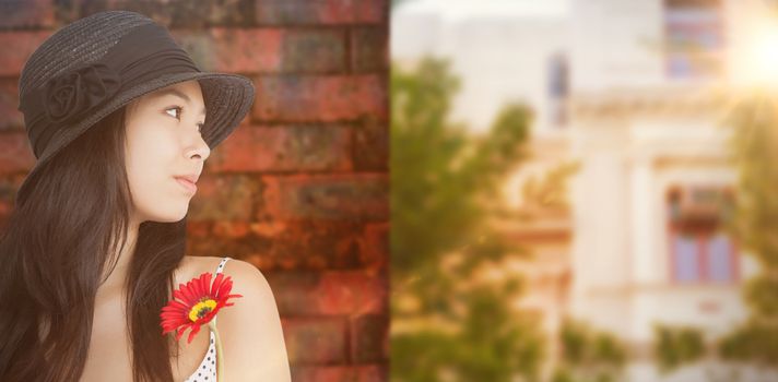 Cheerful woman with flower looking away wearing a hat against wall of a house