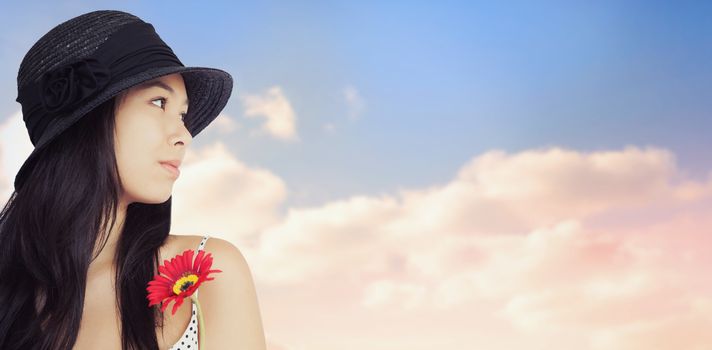 Cheerful woman with flower looking away wearing a hat against beautiful blue cloudy sky