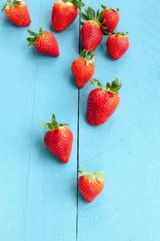 Wild strawberries placed on blue wooden background and illuminated with natural light