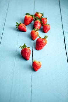 Wild strawberries placed on blue wooden background and illuminated with natural light