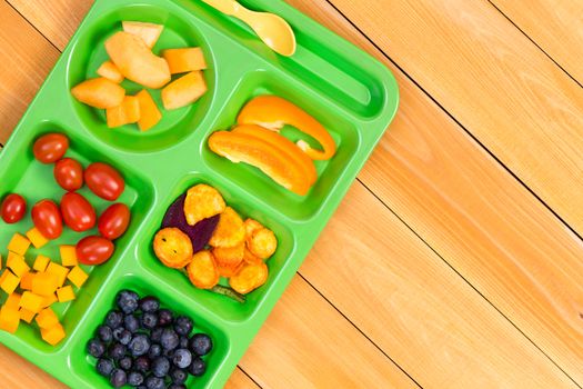 Child size lunch tray with cherry tomatoes, melon, blueberries and sweet pepper fruit on wooden table