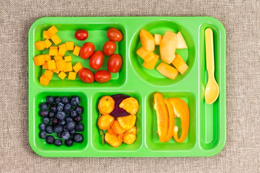 Small rectangular lunch tray with cherry tomatoes, melon, blueberries, sweet pepper and other fruit on surface with cloth texture