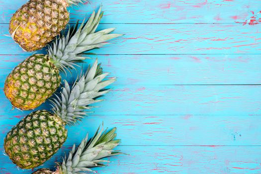 Row of four slanted pineapple fruits laid down on old blue wooden floor or table with copy space