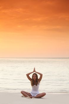 Woman in lotus yoga pose at sunset on the beach