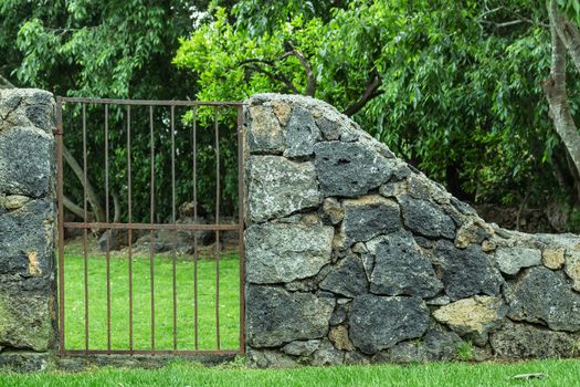 A rustic iron garden gate closing to a lush green lawn.