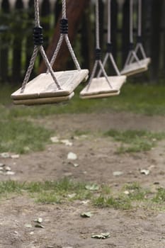 Vertical perspective view of three wooden child swings in the park with shallow depth of field