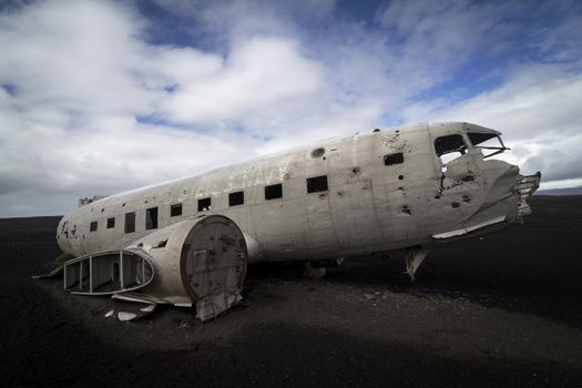 Horizontal side view of a plane wreck on black sands and background of blue sky in south of Iceland