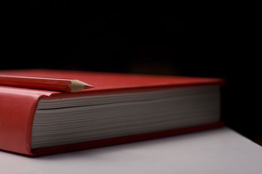 Horizontal side view of a red closed book with a red pencil on top of it