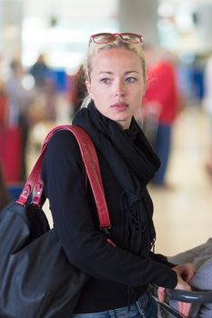 Casual blond young woman using her cell phone while queuing for flight check-in and baggage drop. Wireless network hotspot enabling people to access internet conection. Public transport.