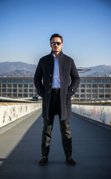 Handsome young man outside wearing winter coat and white shirt, looking at camera, day shot.