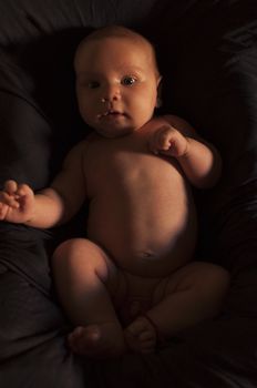 Newborn boy sitting in his crib covered with soft textile