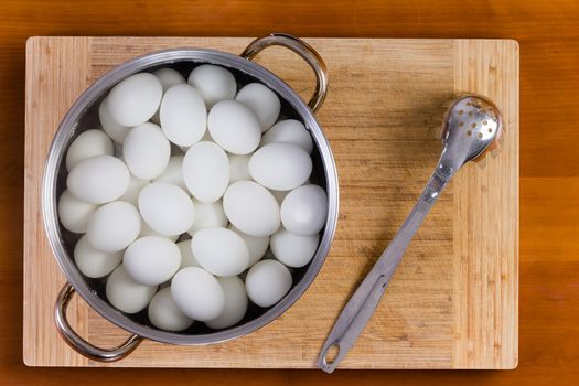 Boiled white hens eggs in a metal saucepan or colander standing on a wooden board cooling for decorating with colored dye for the Easter holiday
