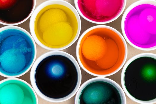 Dyeing hard-boiled hens eggs for Easter with a close up overhead view of fresh white eggs steeping in individual jars of dye to soak up the colors, full frame view