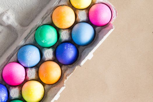 Vibrant hand dyed colorful Easter eggs in a cardboard egg box viewed from above on a beige background with copy space for your greeting