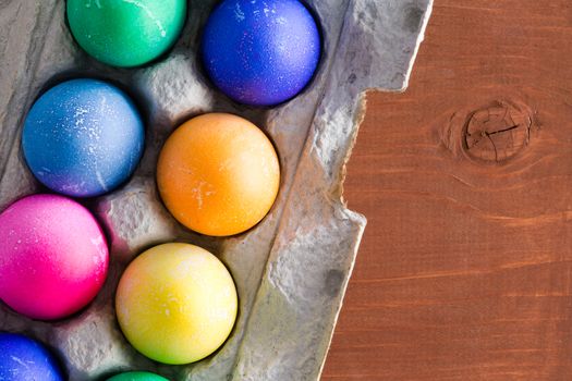 Fun traditional vibrant hand dyed Easter eggs in a close up view from above in a cardboard egg box on a wooden table with copy space for your seasonal message