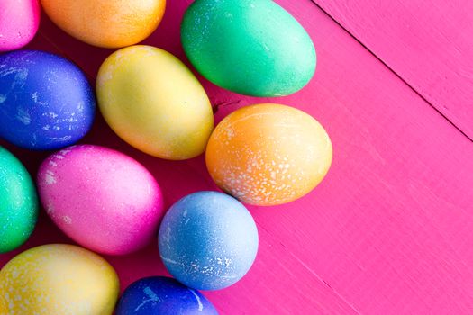 Cluster of colored dyed natural hens eggs for Easter in the colors of the rainbow on an exotic vivid magenta pink wooden background with copy space for your holiday greeting