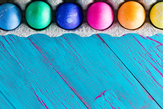 Colorful Easter egg frame on exotic blue crackle painted diagonal wooden boards copy space with a row of hand dyed eggs in a cardboard egg box