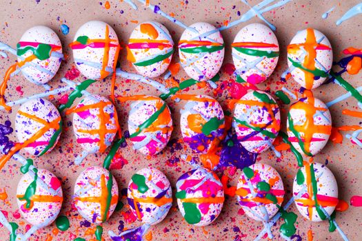 Colorful kids project of hand painted Easter eggs with a random splatter of vibrant paint in pink, orange green and blue splattered on neat white eggs in three rows for a colorful seasonal background