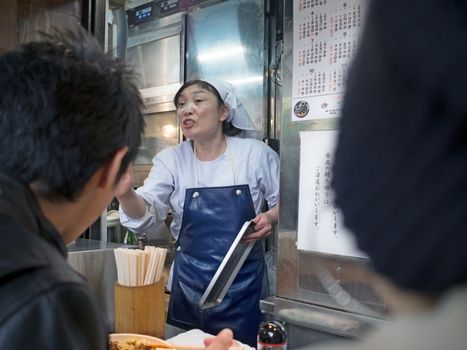 Tokyo, Japan - November 13, 2015: Tsukiji market is  a major tourist attraction, small restaurants surrounding it do brisk business. Female boss with control freak management style running a small tsukiji food restaurant. 