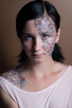 Portrait of a beautiful young girl with creative makeup mask pattern of bright colors.