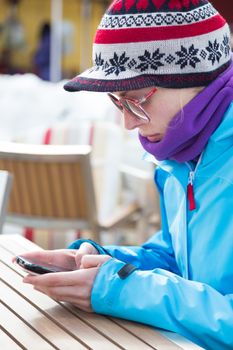 Woman on winter vacations in ski resort texting using smartphone.