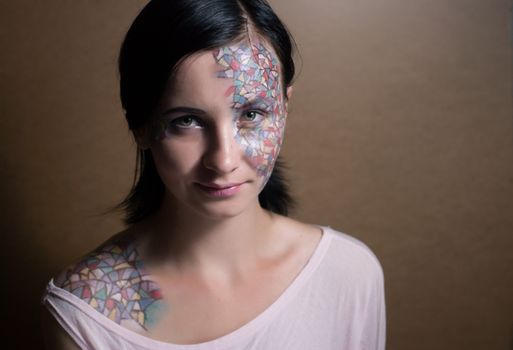 Portrait of a beautiful young girl with creative makeup mask pattern of bright colors.