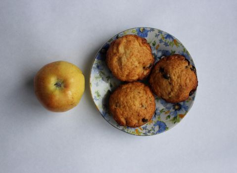 still life: three cupcake with raisins on a blue dish and apple on a white background.