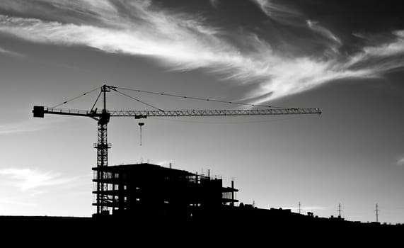 A black and white picture of construction crane under sky with clouds. 