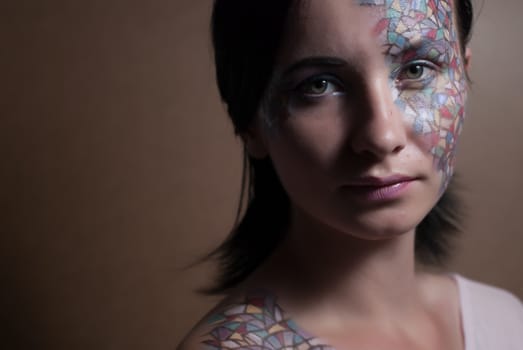 Portrait of a beautiful young girl with creative makeup mask pattern of bright colors.